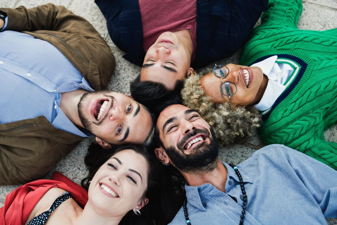 A diverse group of friends lying in a circle outdoors, laughing together